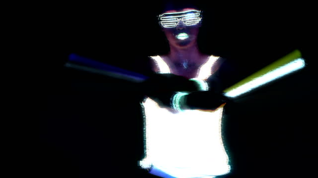 Woman-with-UV-face-paint,-glowing-clothing,-glowing-glasses,-bracelet-dancing-in-front-of-camera-holding-chemical-light,-half-body-shot.-Asian-woman.-Glitch-effect.-Women.