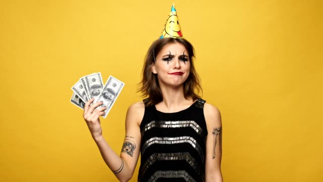 Carefree-lady-with-halloween-make-up-holding-in-hands-candies-and-money-and-choose-money-isolated-over-yello