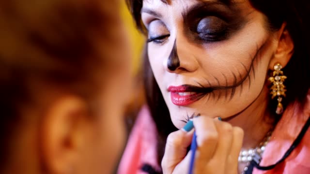 Halloween-Party,-Make-up-Artist-zieht-eine-schreckliche-Make-up-auf-dem-Gesicht-eine-Brünette-Frau-für-eine-Halloween-Party.-im-Hintergrund-sieht-man-die-Landschaft-im-Stil-von-Halloween