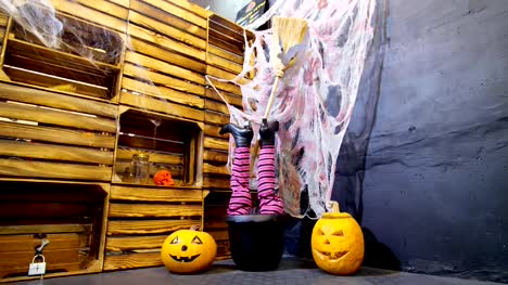 Halloween-Party,-Landschaft-im-Stil-von-Halloween-mit-Kürbissen,-Spinnweben.-in-einem-Kessel,-Topf,-Frauen-die-Beine-durchhalten-in-Stiefeln-und-einem-Besen-einer-Hexe
