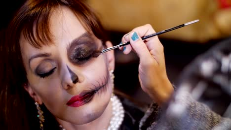 Halloween-Party,-close-up,-Make-up-Artist-zieht-eine-schreckliche-Make-up-auf-dem-Gesicht-eine-Brünette-Frau-für-eine-Halloween-Party.-die-Landschaft-im-Stil-von-Halloween-gesehen