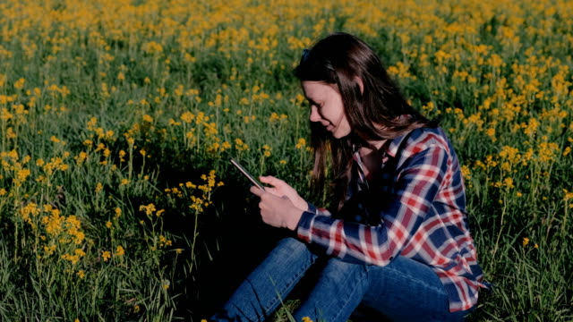 Frau-Handy-sitzen-im-Park-auf-dem-Rasen-unter-den-gelben-Blüten-betrachten.