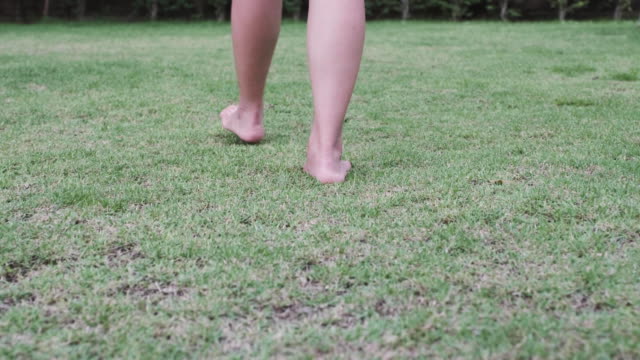 A-woman-walking-barefoot-on-the-green-yard-alone