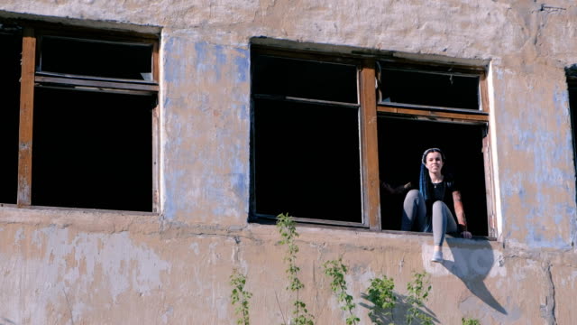 Woman-sitting-on-window-of-destroyed-multi-storey-building-with-many-broken-windows.