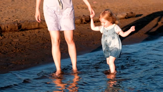 Mutter-und-Mädchen-spielen-am-Strand-des-Flusses-bei-Sonnenuntergang-und-Schwimmen.
