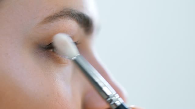 Extreme-close-up-visagiste-applying-eye-shadows-using-cosmetic-brush-to-face-teenage-model