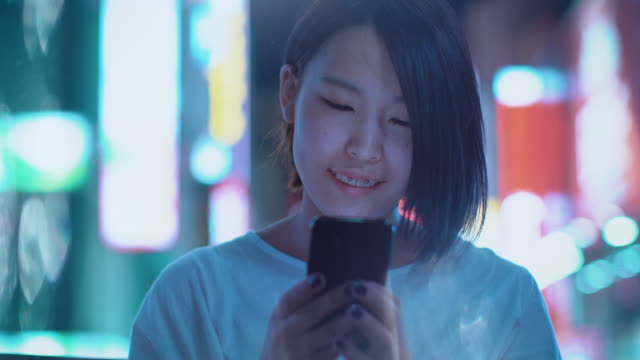 Portrait-of-the-Attractive-Japanese-Girl-with-Piercing-and-Wearing-Casual-Clothes-Uses-Smartphone.-In-the-Background-Big-City-Advertising-Billboards-Lights-Glow-in-the-Night.