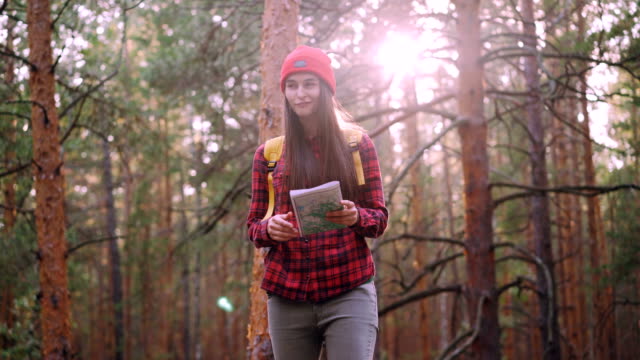 Happy-tourist-attractive-young-woman-is-travelling-in-forest-then-looking-at-map-and-looking-around-exploring-wood.-Adventurous-people,-happiness-and-sunlight-concept.