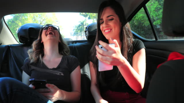 Real-life-laugh-of-friends-together-in-the-back-seat-of-a-taxi-holding-cellphones-and-checking-messages.-Candid-clip-of-two-girlfriends-interacting-with-online-content