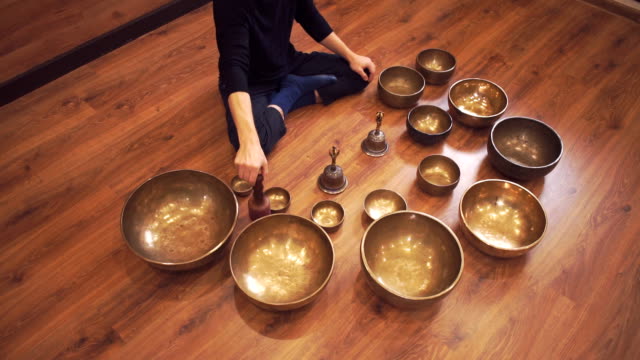 A-man-sits-on-the-floor-in-the-lotus-position-and-plays-on-the-Tibetan-bowls