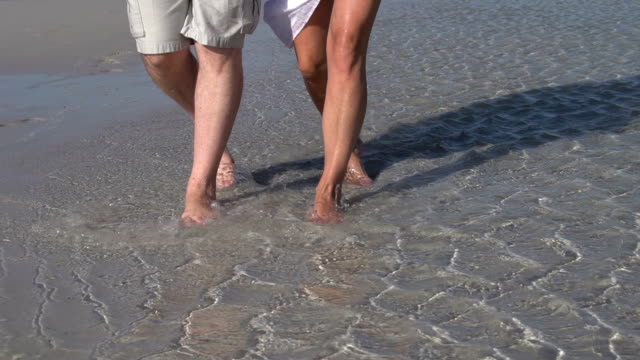 Cámara-lenta-Recortar-imagen-de-patas-de-Pareja-caminando-por-el-agua-en-la-playa,-Sudáfrica