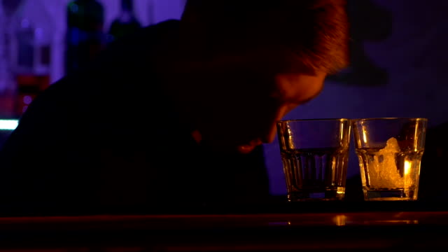 Young-bartender-making-tricks-with-two-glasses-and-puts-ice--standing-behind-the-bar,-shots,-slow-motion