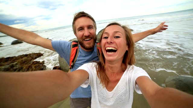 Young-couple-stand-near-Moeraki-boulders-and-take-selfie-portrait