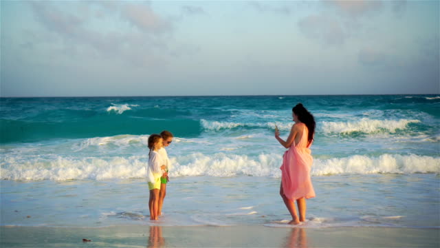Junge-Mutter-machen-Foto-auf-Handy-ihrer-Kinder-am-Strand-im-weichen-Abendlicht