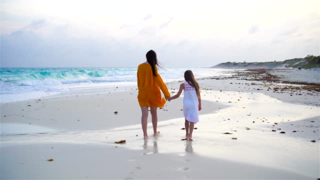 Little-adorable-girl-and-young-mother-at-tropical-beach-in-warm-evening