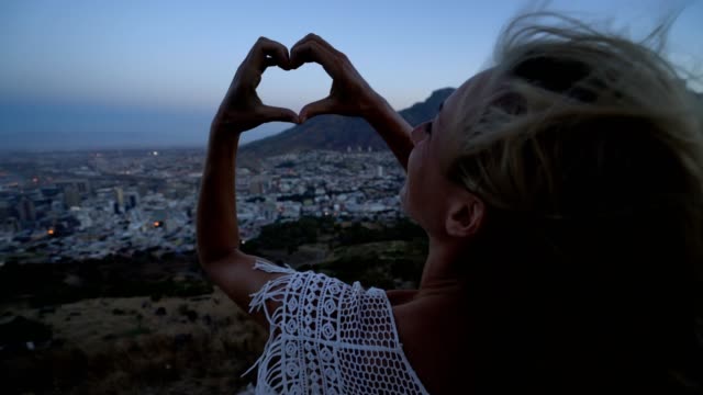Young-woman-making-heart-shape-frame-in-Cape-Town-at-sunrise