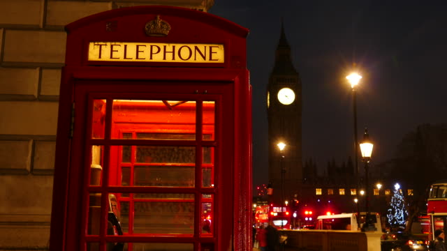 Una-cabina-de-teléfono-rojo-icónico-frente-el-Big-Ben-y-del-Parlamento-en-Londres,-Reino-Unido-en-la-noche.
