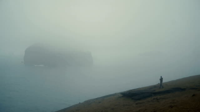 Young-woman-standing-on-the-shore-of-the-sea-in-foggy-day-and-enjoying-the-view-in-Iceland,-thinking-about-something