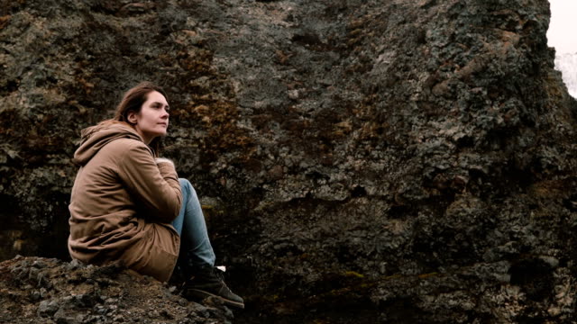 Junge-schöne-Frau-sitzt-auf-dem-Felsen-in-Bergen-und-denken-allein.-Touristen,-die-Ruhe-nach-dem-Wandern-in-Island