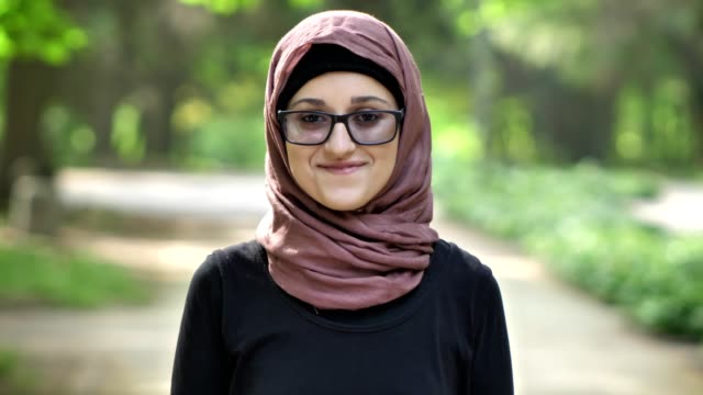 Porträt-eines-lachenden-Mädchens-in-Gläsern-tragen-Hijab,-im-Freien,-in-einem-Park-im-Hintergrund.-50-fps