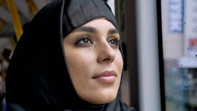 Gesicht-des-jungen-süßen-Muslima-Hijab-ist-gerade-im-verregneten-Fenster-im-Bus,-Transportkonzept,-städtebauliche-Konzept,-Wetter-Konzept,-Konzept-träumen