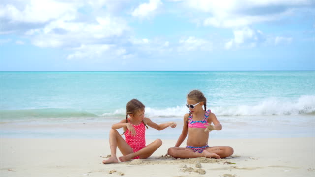 Zwei-kleine-glückliche-Mädchen-haben-eine-Menge-Spaß-am-tropischen-Strand-mit-Sand-spielen