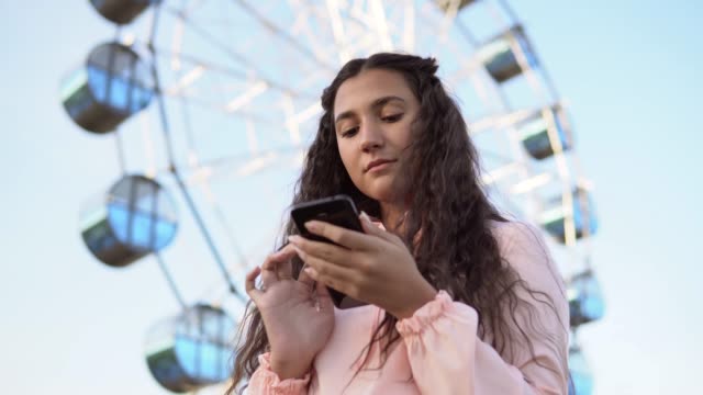 The-girl-is-using-a-smartphone-standing-near-the-Ferris-wheel-.4K.-Close-up