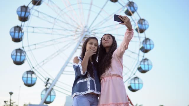 Zwei-schöne-Freundinnen-machen-eine-Selfie-im-Hintergrund-von-einem-Riesenrad.-4K