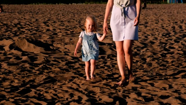 Schöne-blonde-Mutter-und-Tochter-Fuß-am-Strand-bei-Sonnenuntergang.