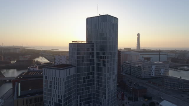 Aerial-4K:-Skyscraper-office-building-in-Malmö-city-at-sunset.-Drone-shot-flying-over-city-and-street-and-backwards,-modern-financial-business-district