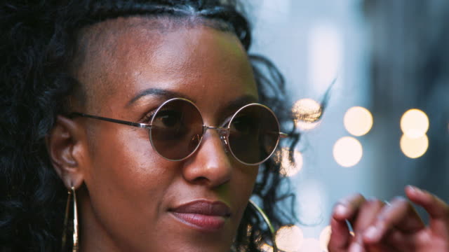 Fashionable-young-black-woman-wearing-sunglasses-looking-up,-head-shot,-bokeh-lights-in-background