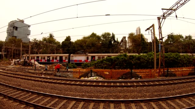 few-people-work-in-distance-on-local-railway-lines-train-goes-behind-background-of-many-storied-houses