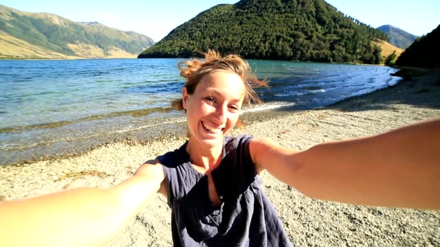 Cheerful-young-woman-takes-a-selfie-portrait-by-the-lake