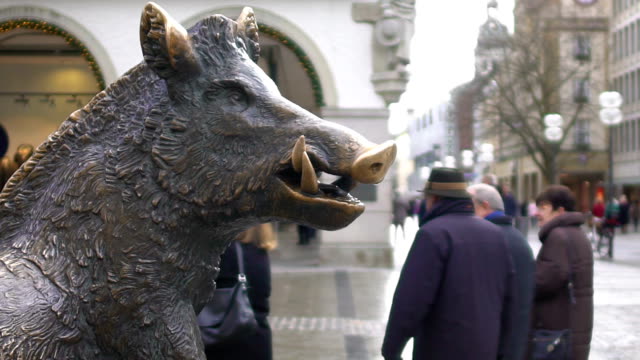 Bronze-statue-of-wild-boar-in-historical-city-center,-tourists-walking-around