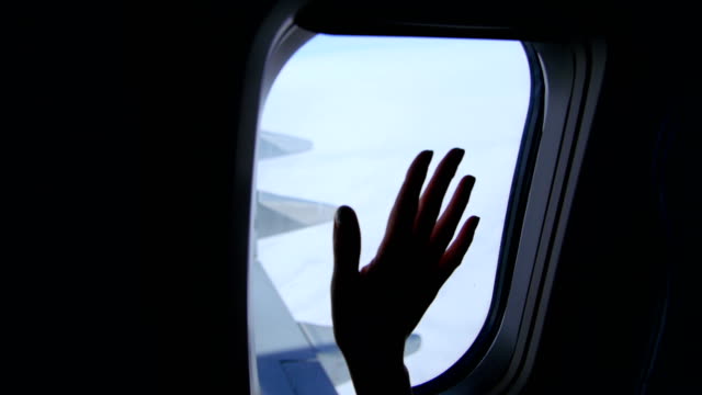 View-from-the-airplane-window,-you-can-see-the-dark-silhouette-of-the-female-hand,-the-palm,-the-movement-of-the-fingers,-the-sky,-the-clouds,-the-wing-of-the-plane.-The-weather-is-clear,-sunny