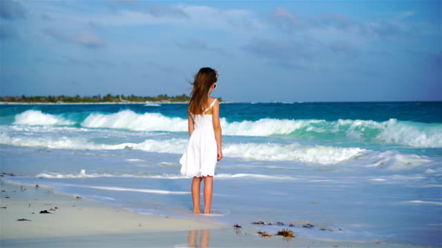 Liebenswert-glückliches-kleines-Mädchen-auf-weißen-Strand-mit-Blick-auf-den-Ozean.-Laut-Meer-und-einem-kleinen-niedlichen-Kind