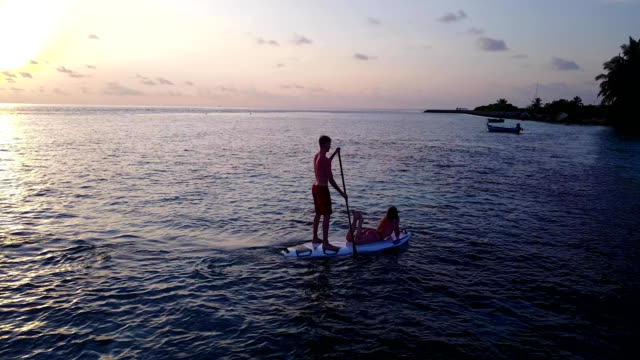 v04106-fliegenden-Drohne-Luftaufnahme-der-Malediven-weißen-Sandstrand-2-Personen-junges-Paar-Mann-Frau-Paddleboard-Rudern-Sonnenuntergang-Sonnenaufgang-auf-sonnigen-tropischen-Inselparadies-mit-Aqua-blau-Himmel-Meer-Wasser-Ozean-4k