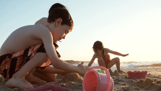 Three-kids-playing-on-the-beach-building-sand-castles-together