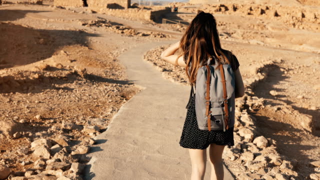Frau-mit-Rucksack-erkundet-Wüste-Ruinen.-Schöne-europäische-touristische-Spaziergänge-auf-Felsen-und-Sand.-Masada-Israel-4K