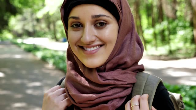 Porträt-eines-lächelnden-Mädchens-in-einem-Hijab-steht-im-Wald-mit-einem-Rucksack-Reisen-Konzept-50-fps