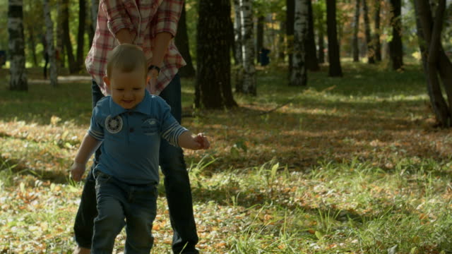Beautiful-young-mother-and-her-adorable-toddler-son-having-fun-together-in-autumn-park,-boy-is-running-from-his-mommy