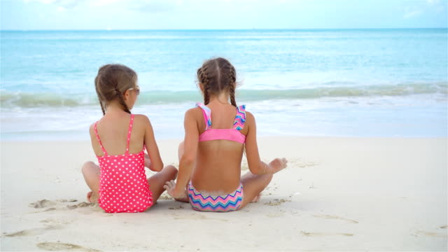 Zwei-kleine-glückliche-Mädchen-haben-eine-Menge-Spaß-am-tropischen-Strand-mit-Sand-spielen