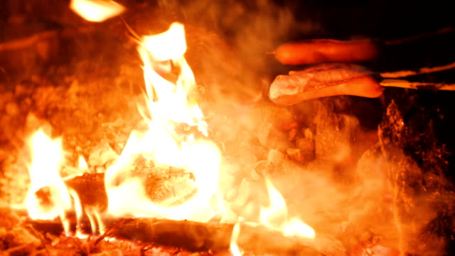 People-fry-sausages-on-a-fire-in-the-woods-at-night.-Close-up-sausages.