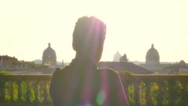 Beautiful-young-woman-walking-toward-high-balcony-in-campidoglio-to-see-cityscape-of-Rome-at-sunset-viewing-historic-buildings-and-domes-slow-motion-steadycam
