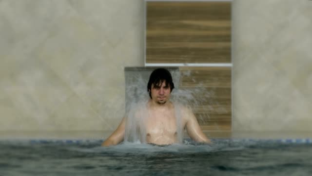 Junger-Mann-genießen-Pool-Spa-Tag-im-erholsamen-Urlaubsort.-Hydro-Massage-für-Nackenschmerzen.-Unter-Wasser-Jet,-Nacken-und-Wirbelsäule-Massage-entspannen.