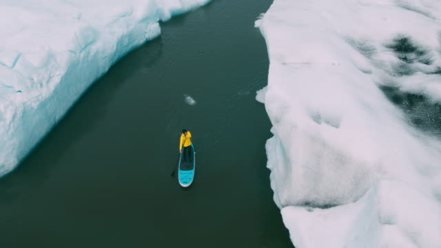 Abenteuerliche-Jüngling-Paddeln-Stand-up-Paddle-boarding-durch-Eisberge-im-Gletschersee-in-Island