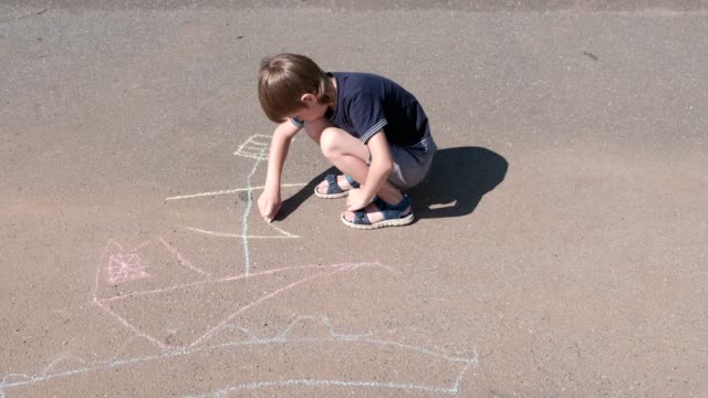 Boy-draws-a-ship-with-blue-chalk-on-the-asphalt.-Close-up-hands.