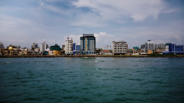 Drone-flying-low-above-the-ocean-water-towards-Colombo-city-coastline,-Sri-Lanka,-modern-buildings-on-the-shore-line