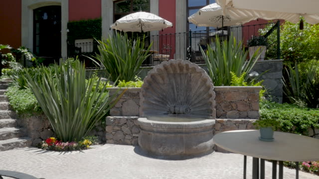 Outdoor-patio-and-garden-with-a-shell-fountain-and-tables-with-umbrellas