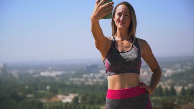 junge-Frau-in-ihre-Trainingskleidung-unter-malerischen-Selfies-mit-ihrem-Handy